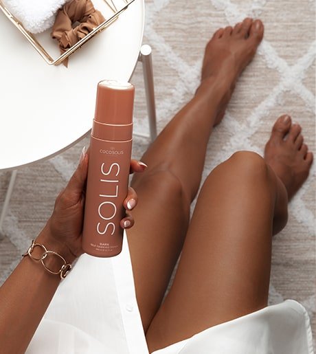 A woman displaying the COCOSOLIS SOLIS Self-Tanning Foam with beautifully tanned legs